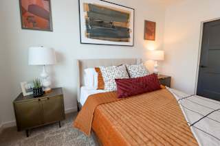 Bedroom with orange bedding and framed artwork at The Wren Apartments, Lawrenceville, GA 30043
