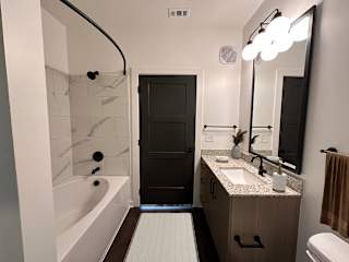 A bathroom with a marble tub surround and a black door at The Wren Apartments, Lawrenceville  30043
