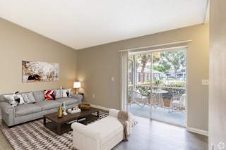 A living room with a grey couch, a coffee table, and a painting on the wall. at Aqua Bay Apartments in Naples, FL 34116