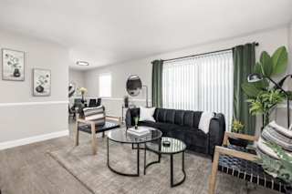 A living room with a black couch, a glass table, and a grey rug.