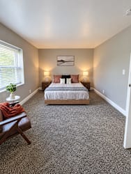 A bedroom with a bed, two lamps, a chair, and a painting on the wall.