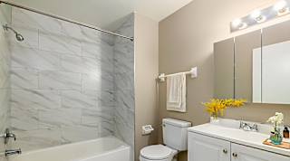 A bathroom with a marble tile shower, white bathtub, toilet, and sink.