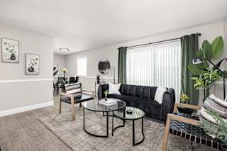 A living room with a black couch, a glass table, and a rug.