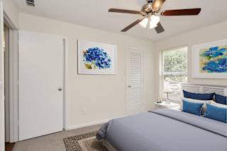 A bedroom with a bed, pillows, a ceiling fan, and two framed pictures on the wall. at Aqua Bay Apartments in Naples, FL 34116