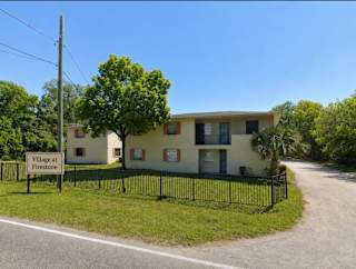 A sign that says "Village at Firestone" stands in front of a building.