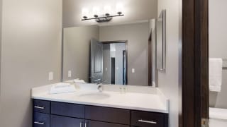 Furnished apartment bathroom with dark finish cabinetry for storage and large mirror