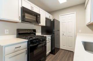 newly renovated kitchen featuring black appliances, white cabinets, quartz countertops, and luxury vinyl planking