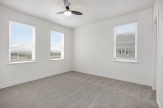 an empty living room with three windows and a ceiling fan