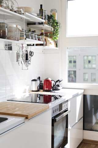 a kitchen with white cabinets and a white stove top oven with a wooden cutting board on top