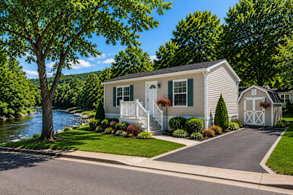 Floor Plan  A house with a white fence and green shutters is situated by a river.