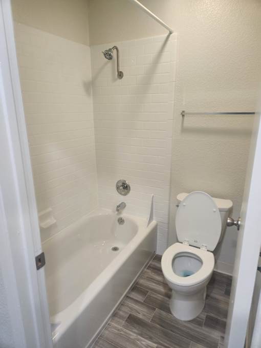 A white toilet is in a bathroom with a white tub and a shower.