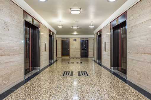 A long hallway with marble floors and doors on both sides.
