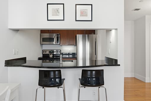 A modern kitchen with a black countertop and two black chairs.