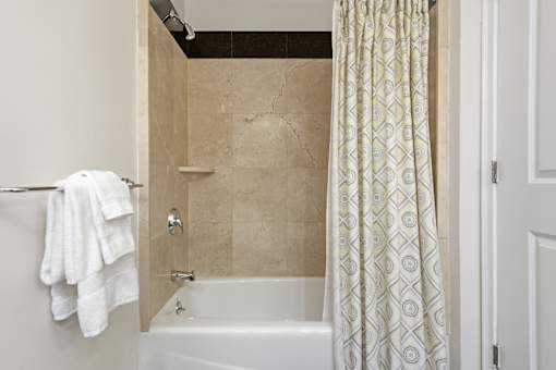 A white bathroom with a tub, towel, and shower curtain.