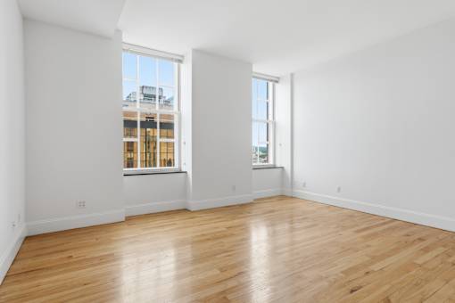 A large empty room with wooden floors and two windows.