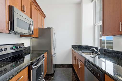 A kitchen with a black counter top and stainless steel appliances.