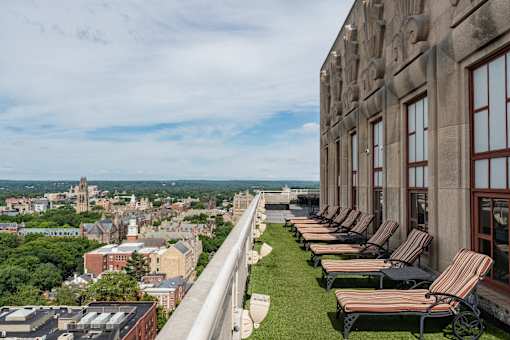 A row of lawn chairs are lined up on a patio overlooking a city.