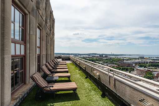 A row of lounge chairs are on a grassy area on a balcony overlooking a city.