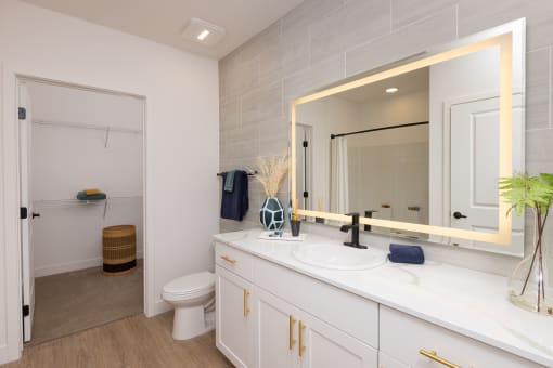 a bathroom with white cabinets and backlit mirror on the wall