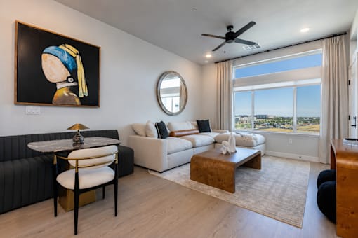 A model apartment living room with large windows,  furniture and a ceiling fan at Amara of a woman, a black sofa, a white couch, a coffee table, and a view of the city.