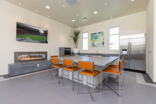 clubhouse kitchen with large table with orange chairs in a room with a fireplace and television