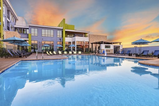 Resort style swimming pool with buildings and sunset in the background at Zeta Luxury Apartments in Sacramento, CA