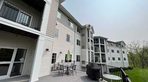 A white two-story apartment building with a balcony and patio furniture.