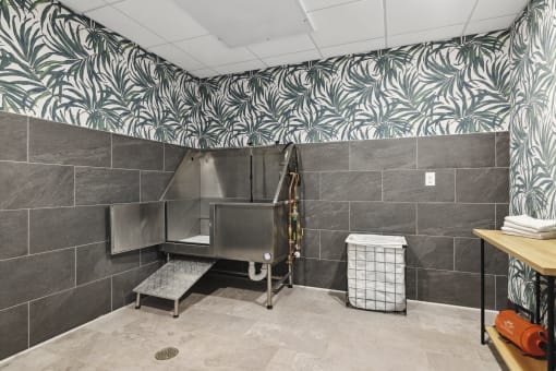a large stainless steel bathtub in a large bathroom with a tropical wallpaper on the wall