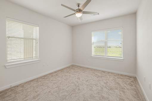 A room with a ceiling fan and two windows.