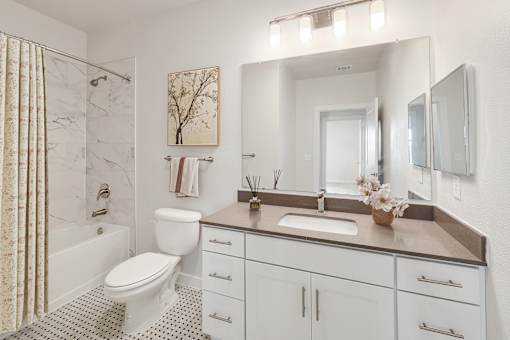 A white bathroom with a marble shower and a brown counter.