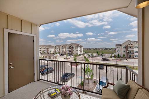 A balcony with a table and chairs overlooking a parking lot and other houses.
