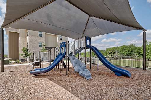 A playground with a blue slide and a grey canopy.