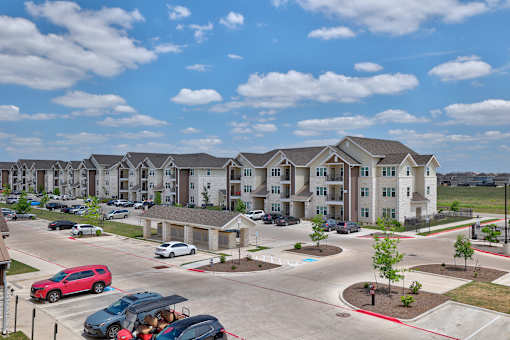 A red car is parked in a parking lot in front of apartment buildings.