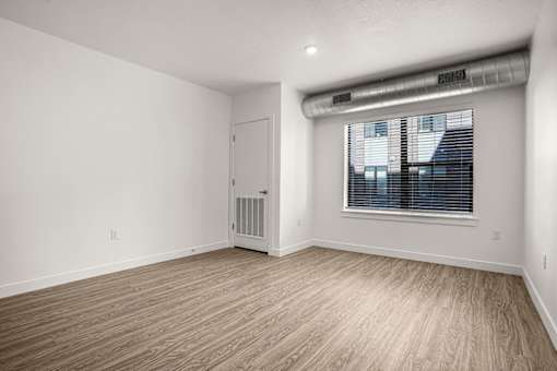 A room with a white door, a window with blinds, and a wooden floor.