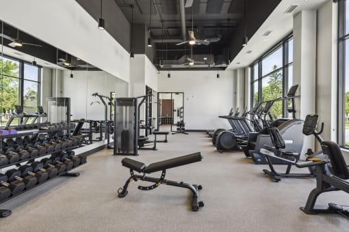 the gym with cardio equipment and weights in a building with windows