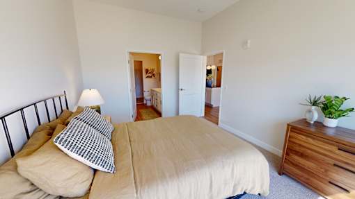 A bedroom with a bed, nightstand, and a plant.