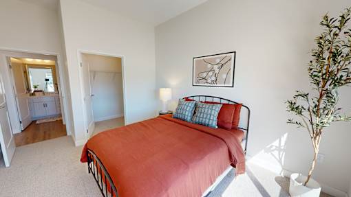 A bedroom with a red bed and a plant on the side table.