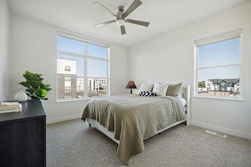 A bedroom with a bed, a ceiling fan, and a window overlooking a cityscape.