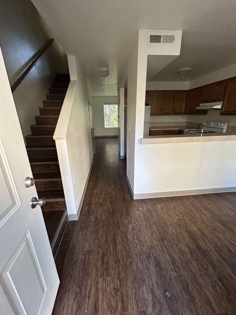 A white door is on the left of a hallway with wooden floors and a staircase.