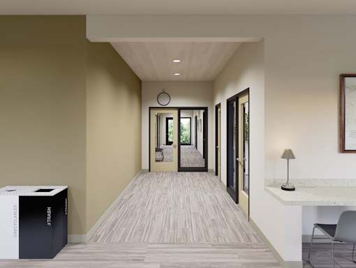 A hallway with a chair, a table, and a trash can.