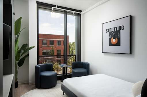 A bedroom with a bed, two chairs, and a poster with the word at Miles at Ybor Apartments, Florida, 33605