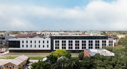 A large white building with a red roof is surrounded by trees at Miles at Ybor Apartments, Tampa, FL, 33605