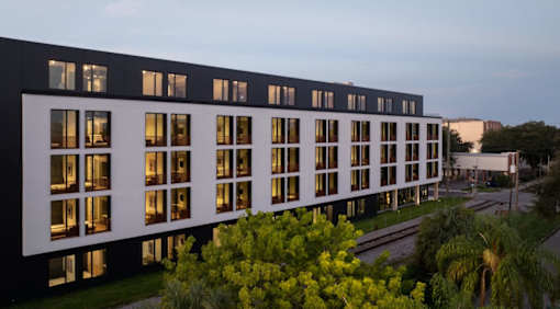 A modern building with a black and white facade is surrounded by greenery at Miles at Ybor Apartments, Florida