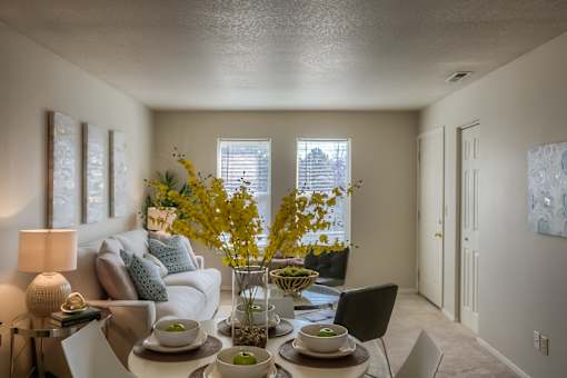 A dining room with a table set for two and a couch with pillows.