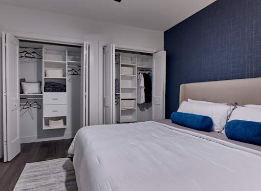 A bedroom with a bed, two nightstands, and a wardrobe with clothes hanging on it.