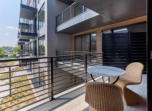 A balcony with a table and two chairs overlooks a garden.