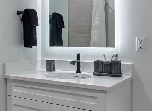 A bathroom with a white countertop and a black faucet.