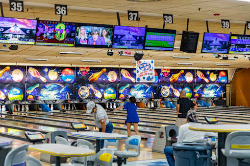 A bowling alley with people playing and a row of monitors above.
