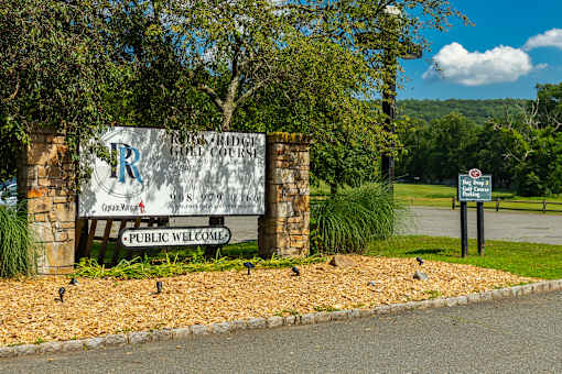 A sign for a public golf course with a phone number and a stop sign in the background.