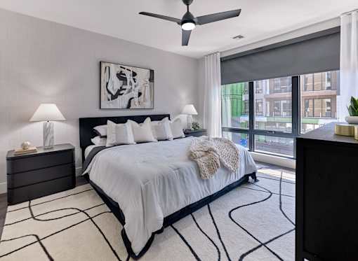 A bedroom with a large bed, a ceiling fan, and a painting on the wall.